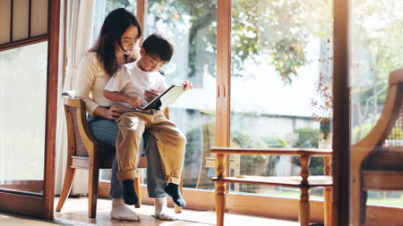 Reading, study or tablet with mother and son on chair in home for child development or learning. Education, Japanese family or technology with single parent woman and boy in apartment for searchの写真素材