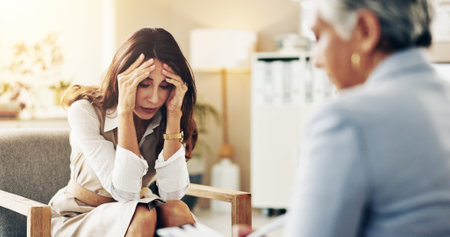 Discussion, therapist and patient with stress in office for mental health or anxiety at appointment. Conversation, medical and mature woman talk to psychologist for advice in consultation at clinic.の写真素材