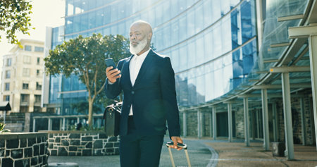 Phone, business and black man with luggage in city for journey, travel schedule or booking flight. Suitcase, walking and mature professional with mobile at building, hotel or trip outdoor on commuteの写真素材