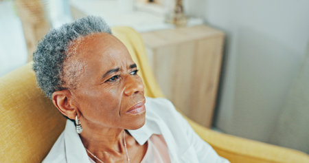 Thinking, sad and elderly black woman in home with depression, nostalgia and reflection in living room. Sofa, retirement and senior person with thoughtful, memory and mourning expression in houseの写真素材