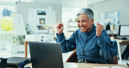 Mature woman, celebration and winning with laptop for good news, promotion or email at office. Excited, female person or employee with smile on computer for amazing offer, deal or prize at workplaceの写真素材
