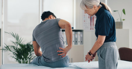 Back pain, physical therapy and patient at consultation for problem, inflammation or muscle strain. People, chiropractor and treatment for injury, rehabilitation and recovery of spinal ligamentsの写真素材