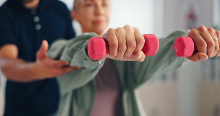 Physiotherapy, woman or hands with dumbbells for rehabilitation, muscle exercise or body health. Mobility, client or stretching with light weights for fitness, physical recovery or help with balanceの写真素材