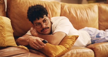 Relax, TV and man on sofa with remote for watching movies, film and series for lazy weekend. Living room, chill and person on couch for videos, entertainment and streaming subscription at homeの写真素材