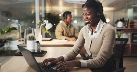 Happy woman, call center and typing on laptop for telemarketing, business and laughing. Help, insurance and African agent on computer for customer service, funny joke and crm at night on deadlineの写真素材