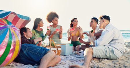 People, friends and watermelon at beach, picnic and conversation with eating, vacation and reunion. Group, women and men with fruit, happy and outdoor together with diversity by ocean in sunshineの写真素材