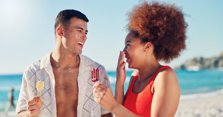 Couple, ice cream and laugh on vacation at beach in summer, bonding and interracial love with funny chat. People, man and woman with desert, memory or comic conversation on holiday with walk by oceanの写真素材