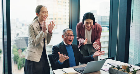 Business people, applause and team celebrate on laptop for achievement, success or clapping. Excited, winner or mature manager cheers with Japanese group for award, yes or investment profit in officeの写真素材