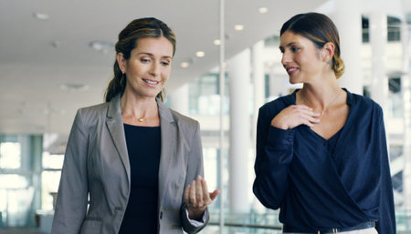 Business women, attorney and talking in office building for walking, together or discussion in law firm. Female people, colleagues and mentorship as lawyer for teamwork, conversation or collaborationの写真素材