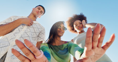 Friends, selfie and gen z people in low angle, blue sky or fashion with attitude for portrait in sunshine. Woman, group and hands for photography, memory or profile picture with streetwear in summerの写真素材