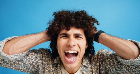Frustrated man, portrait and shouting with afro for bad hair, crisis or mental breakdown on a blue studio background. Male person, gen z or angry model screaming or yelling with curly hairstyleの写真素材