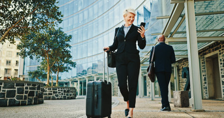 Phone, businesswoman and travel with luggage in city for journey, booking flight or walking. Mobile, trip or mature professional with suitcase at hotel, commute or happy manager reading email onlineの写真素材