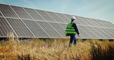 Solar panels, walk and technician with woman in nature for photovoltaic grid, renewable energy or power generator. Sustainability, electric system or inspection with engineer in outdoor for projectの写真素材