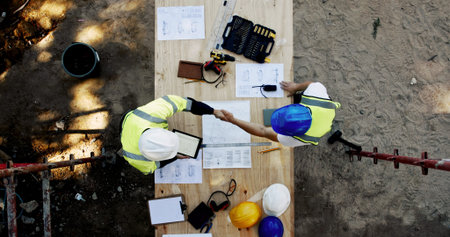 Blueprint, construction and men at table with handshake, collaboration and inspection agreement from...