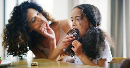 Mother, girl and happy with feeding cupcake at home for bonding, care and support. People, family and parent with kid for eating dessert or food as meal at apartment for fun and child developmentの写真素材