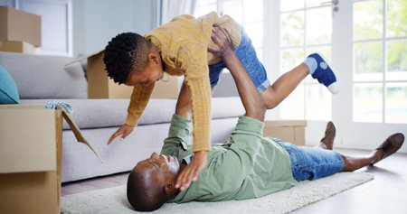 New home, playing or father with child in air for playful bonding, relocation or property on living room floor. Black family, dad and son with smile or boxes for aeroplane, holiday or moving in houseの写真素材