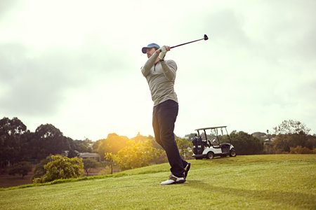 Man, swing and golf on field for sports, cloudy sky and space with equipment, exercise and skill. Male person, golfer and strike club on outdoor course for competition, nature and practice gameの写真素材