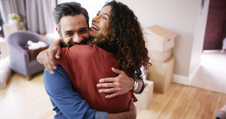 Happy couple, hug and celebrate moving in new home, relocation success and homeowners for mortgage. People, embrace and proud of real estate achievement in living room, support and house securityの写真素材