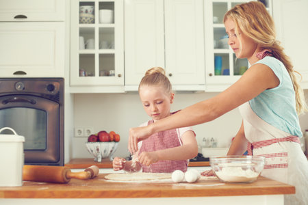 Home, kid and mom with help baking for teaching, learning and happy bonding together for lunch. Love, mother and daughter with rolling pin, ingredients and cookie recipe in kitchen with child bakerの写真素材