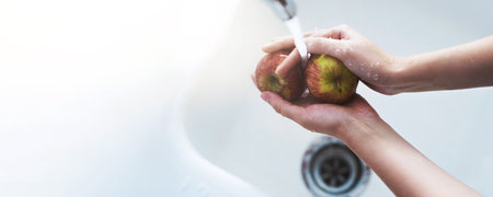 Hands, faucet and washing apples in home for hygiene, dirt or toxic pesticide with banner for safety by sink. Person, fruits and water for cleaning dust, germs or mockup space for snack at apartmentの写真素材