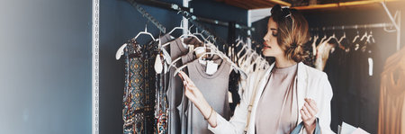Woman, shopping and check price for fashion with thinking, budget or decision on discount at boutique. Person, tag and rack for clothes, sale or deal for choice, banner or customer experience at mallの写真素材