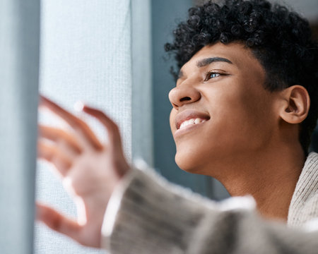 Home, thinking and happy man by window in bedroom with idea, reflection or remember memory. Smile, dream and gen z person for decision, inspiration or planning future in apartment with solutionの写真素材