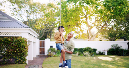 Man, child and rope in garden for swing, DIY games and support in home for protection. Father, son or playing in backyard with bonding, fun activity and help for safety with happiness in relationshipの写真素材