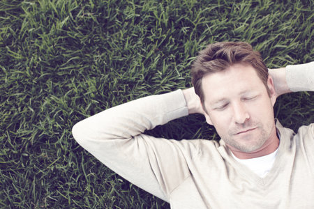 Man, relax and sleeping on grass outdoor for resting, afternoon nap and exhausted in backyard. Calm person, face and dreaming on lawn at park with fatigue, tired and break with top view in natureの写真素材