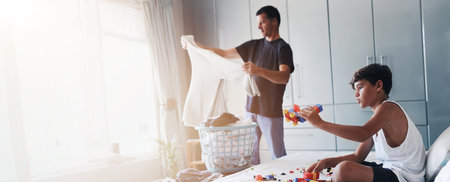 Father, folding and clothes with child playing for cleaning, chores routine and laundry maintenance. Man, boy and household task of hygiene, educational toys and banner for bonding together at houseの写真素材