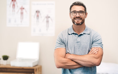 Physiotherapist, portrait and office for sport, exercise or body care in wellness, help or gym at clinic. Male person, happiness and health as physiotherapy, fitness or rehab center with arms crossedの写真素材