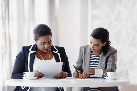 Coffee, documents and business women in office for collaboration on multimedia project together. Research, planning and team of female public relations employees at meeting with creative paperwork.の写真素材