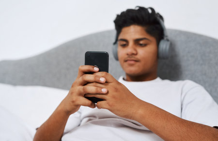 Teenager, headphones and person with phone in home for network, connection and listening to song. Calm, boy and relax with technology in bedroom for audio, streaming and update of music playlistの写真素材