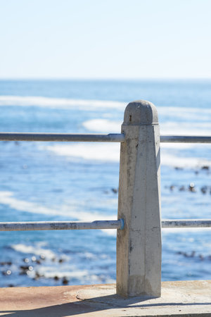 Outdoor, holiday and beach with promenade, railing and destination for travel getaway at sea. Island tourism, nature and ocean with pole or natural waves for paradise or vacation adventure in Greeceの写真素材