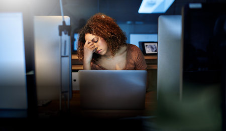 Business, night and woman with headache, laptop and stress with pain, pressure and deadline. Person, evening and employee with migraine, computer or overworked with tension, depression or health riskの写真素材