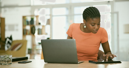 Tablet, laptop and young black woman in the office doing research for creative project. Digital technology, career and professional African female designer working on computer in the modern workplaceの写真素材