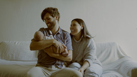 Smile, parents and baby on a sofa in the living room of their home together for love, care or bonding. Family, relax or happy mother and father holding their cute newborn infant chid in a houseの写真素材