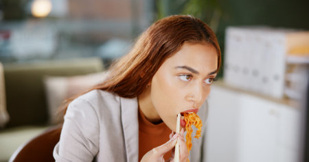 Noodles, desk and business woman with fast food, meal delivery and eating takeout for lunch break. Professional, worker and person with ramen in office for nutrition, wellness and hunger for workingの写真素材