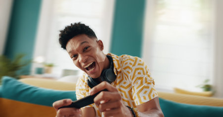Excited man, gamer and sofa with phone for race simulation, entertainment or mobile gaming subscription at home. Portrait, male person or happy player with smile or smartphone for virtual competitionの写真素材