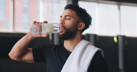 Drinking water, fitness and towel with man in gym for hydration, intense training or workout. Break, exercise and recovery with athlete person in health club for challenge, performance and progressの写真素材