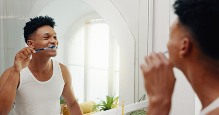 Bathroom, house and man brushing teeth, reflection and hygiene with morning routine. Person, mirror and grooming with toothbrush, fresh breath or cleaning mouth with dental health, smile or whiteningの写真素材