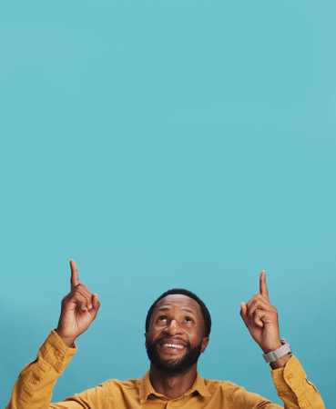 Launch, pointing up or happy black man by space for breaking news, announcement or sales offer. Blue background, choice list or African person in studio with smile for discount mockup, option or menuの写真素材