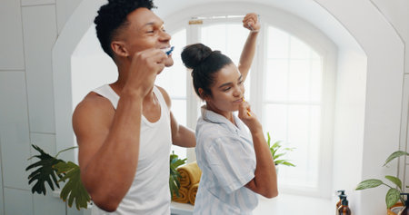 Brushing teeth, dance and morning with couple in bathroom for dental hygiene or oral care. Celebration, love and mirror with playful people having fun in home together to prevent gum diseaseの写真素材
