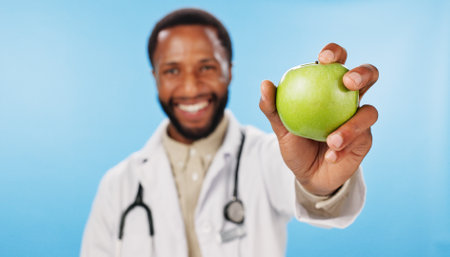 Hand, doctor and happy man with apple in portrait for nutrition, healthcare clinic or healthy food choice. Studio, blue background or nutritionist giving fruit for offer, fibre and vitamin c in dietの写真素材