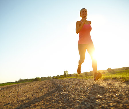 Fitness, woman and running in nature space for cardio training, exercise and morning routine at lens flare. Below, athlete or workout at sky mockup for marathon preparation, healthy body or challengeの写真素材