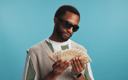 Studio, cash fan or black man with prize, gambling profit and wealth isolated on blue background....