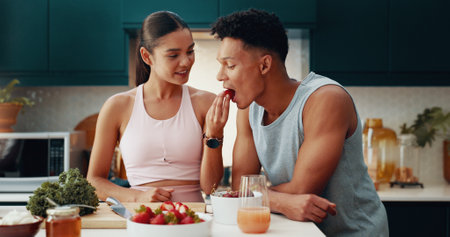 Couple, feeding and fruit for fitness at house of healthy meal, nutrition diet and bonding together. People, eating and strawberry for breakfast snack, morning detox and weight loss of vegan wellnessの写真素材