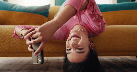 Phone, portrait and woman upside down in home, typing text and post on social media profile on internet. Mobile, face and girl on chat app for communication, check notification and relax on sofaの写真素材
