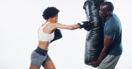 Woman, man and boxer with coach for punching bag, fitness or training for progress by white background. African people, exercise or mentor with martial arts equipment, power or combat sport in studioの写真素材