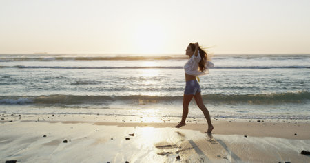 Beach, sunset and travel with woman, vacation and waves with weekend break, carefree and calm. Happy person, outdoor and seaside with girl, summer holiday and adventure with journey, energy or natureの写真素材