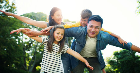 Family, piggyback and outdoor flying for love, fantasy adventure and holiday park for bonding. Happy children, parents and nature for support with airplane games, portrait and together on vacationの写真素材